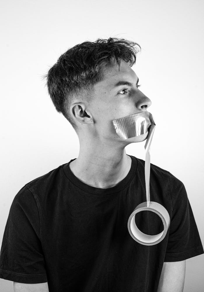 Black and white portrait of a young man with duct tape over his mouth, symbolizing silence.